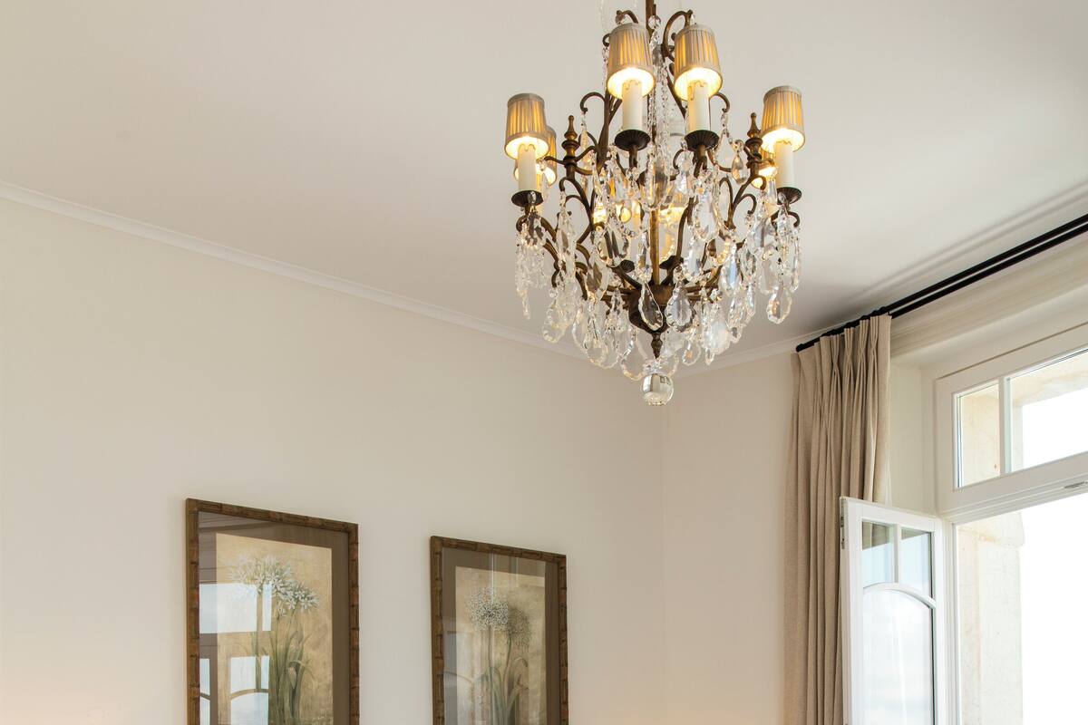 Ein Schlafzimmer mit einem großen Bett, zwei Nachttischen, einer Chandelüster und gerahmten Kunstwerken an der Wand.