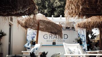 Un club de playa llamado 'GRAND' con asientos al aire libre y sombrillas de paja.