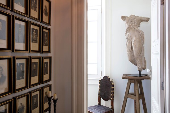 Una habitación con fotografías enmarcadas en la pared, una escultura de busto sobre un pedestal y una silla.