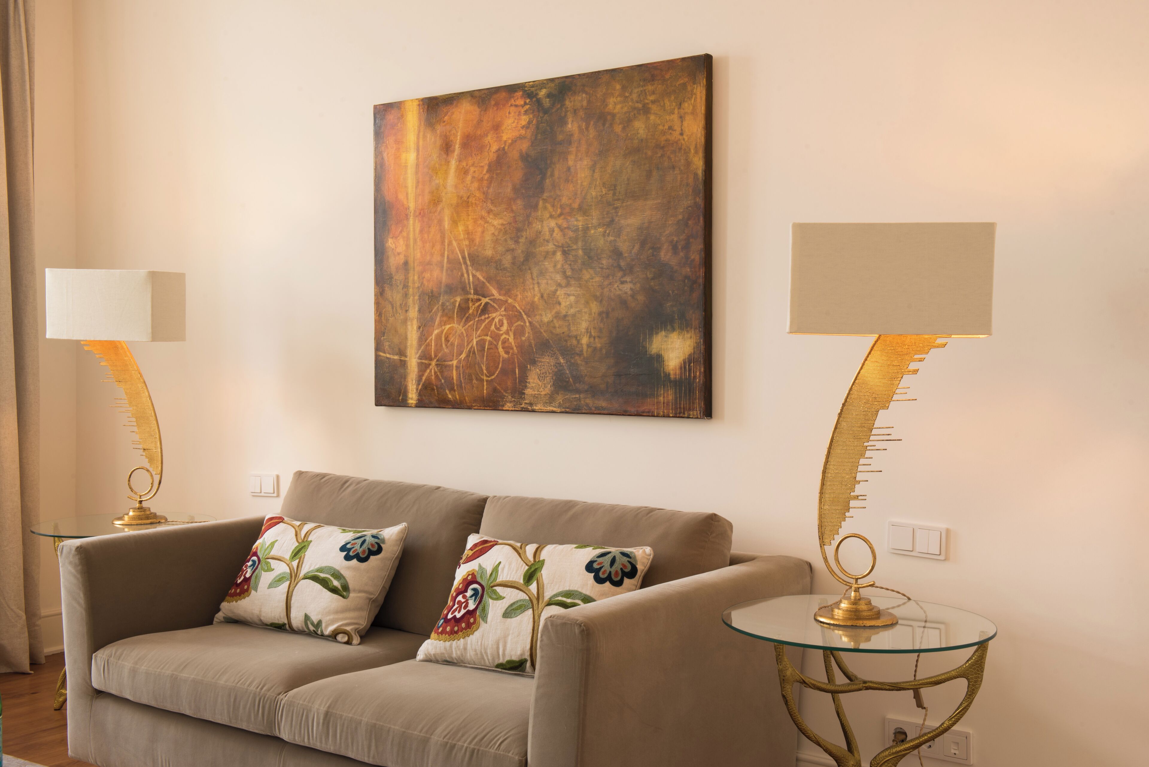 Een woonkamer met een bank, twee lampen en een schilderij aan de muur.