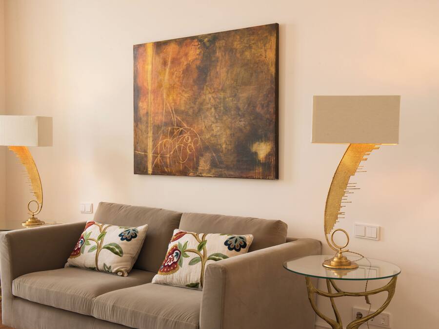 Een woonkamer met een bank, twee lampen en een schilderij aan de muur.