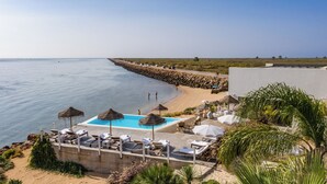 Un espace piscine doté de chaises longues et de parasols, offrant une vue sur la plage et la mer.