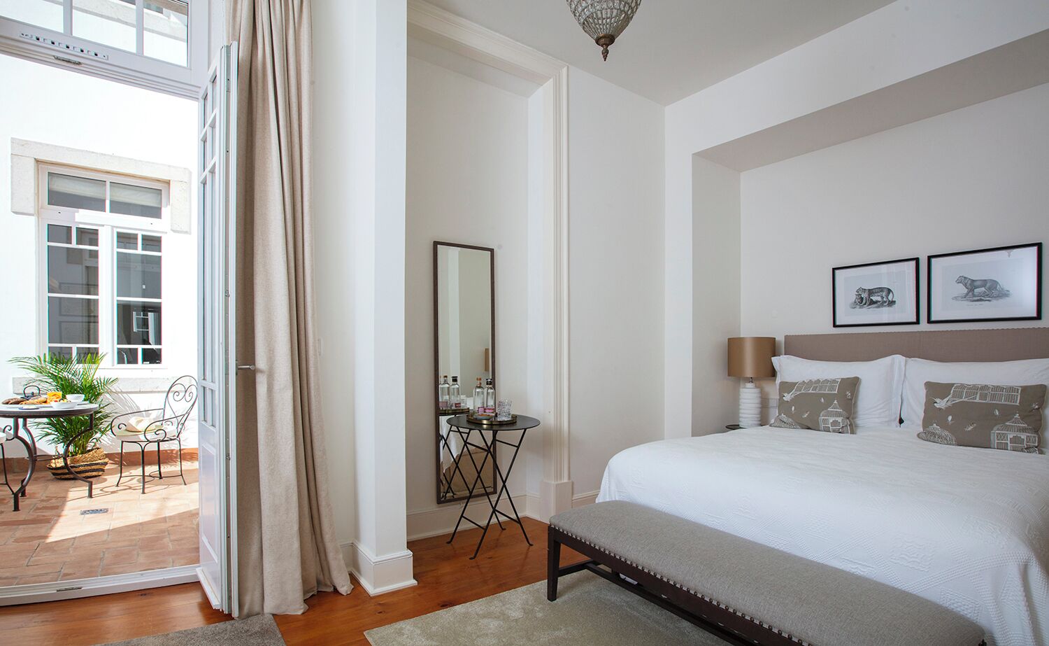 Une chambre à coucher avec un lit, des lampes de chevet, un miroir et une petite table sur laquelle se trouvent une plante et une bouteille.