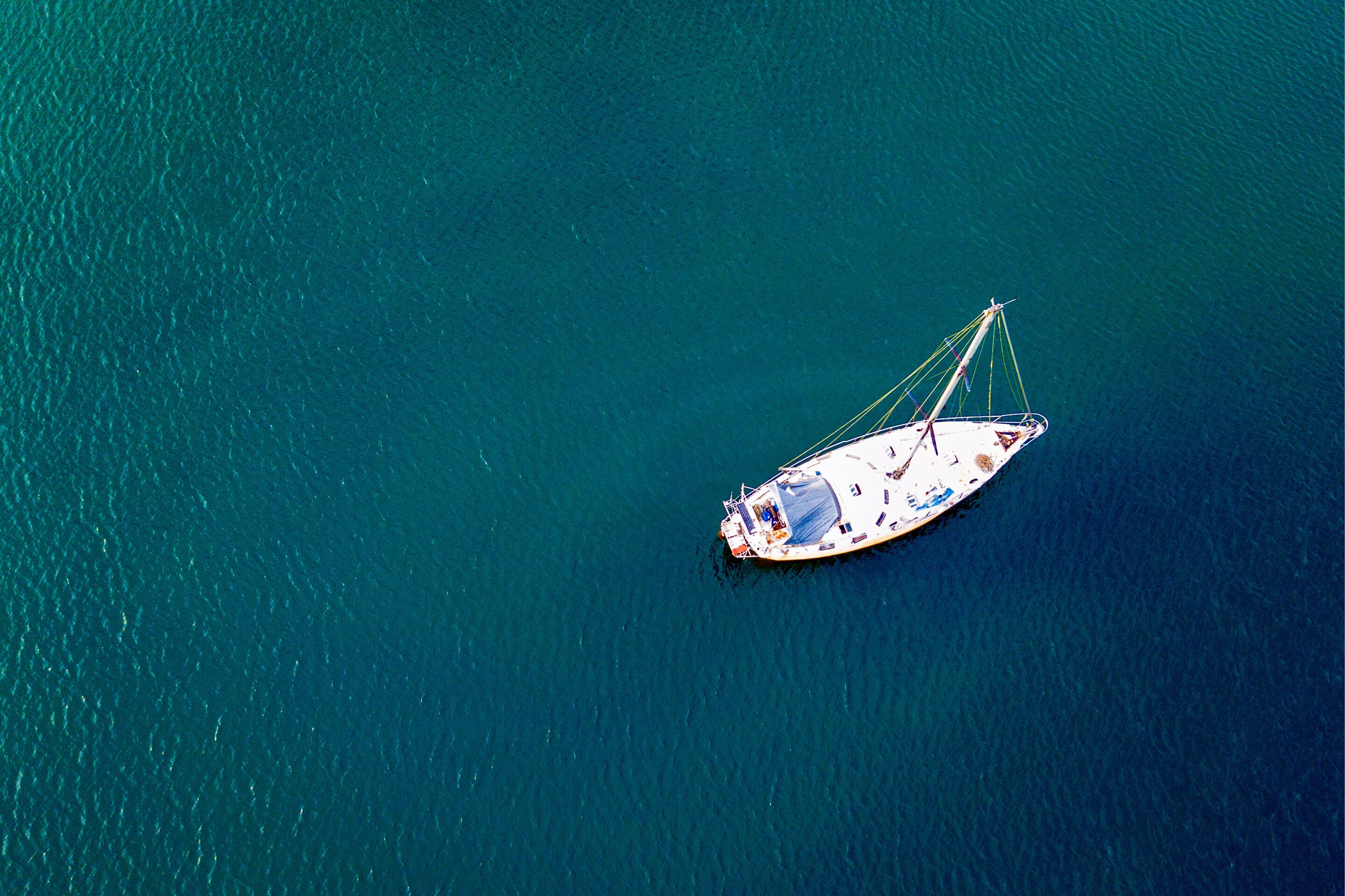 Vista aérea de un velero en aguas turquesas y tranquilas.