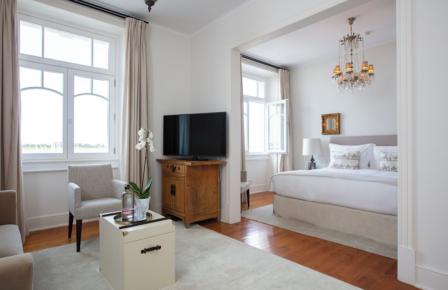 Un dormitorio amplio con una cama grande, televisor, aparador de madera y una araña.