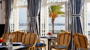 Un coin repas avec des chaises en osier et une table dressée pour deux, donnant sur une étendue d’eau.