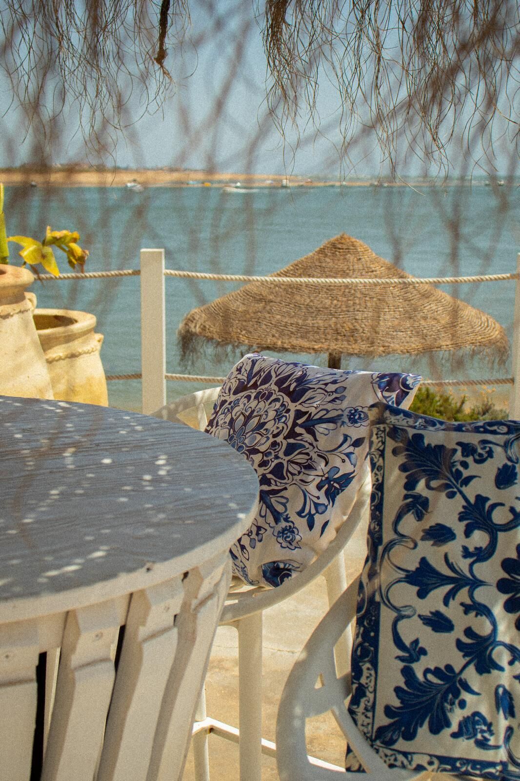 A seaside terrace with a table, chairs, and a patterned vase.