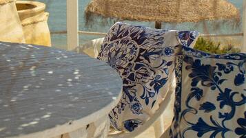 A seaside terrace with a table, chairs, and a patterned vase.