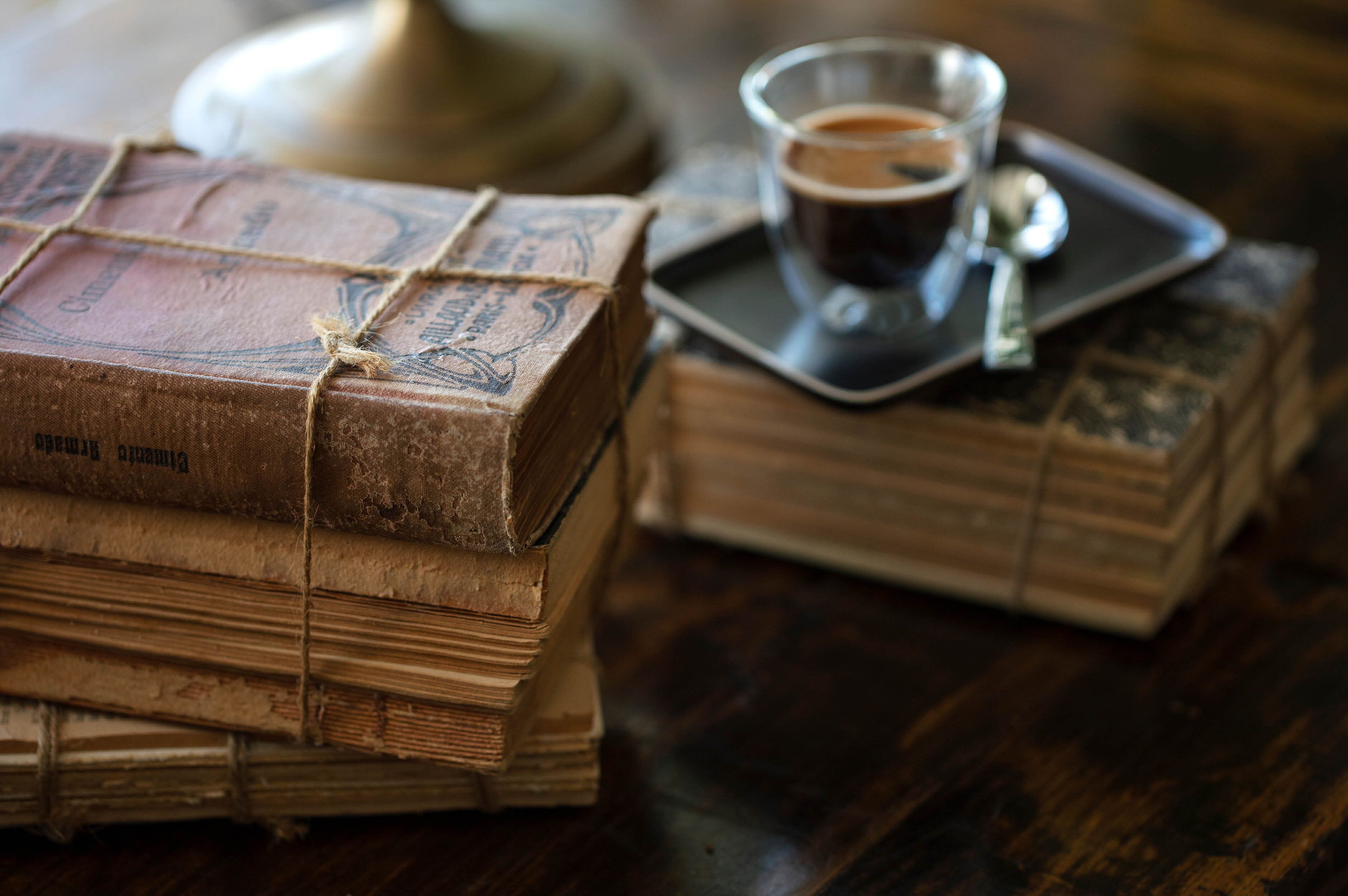 Een stapel oude boeken vastgebonden met touw, een glas koffie en een dienblad met een beker koffie op een houten tafel.
