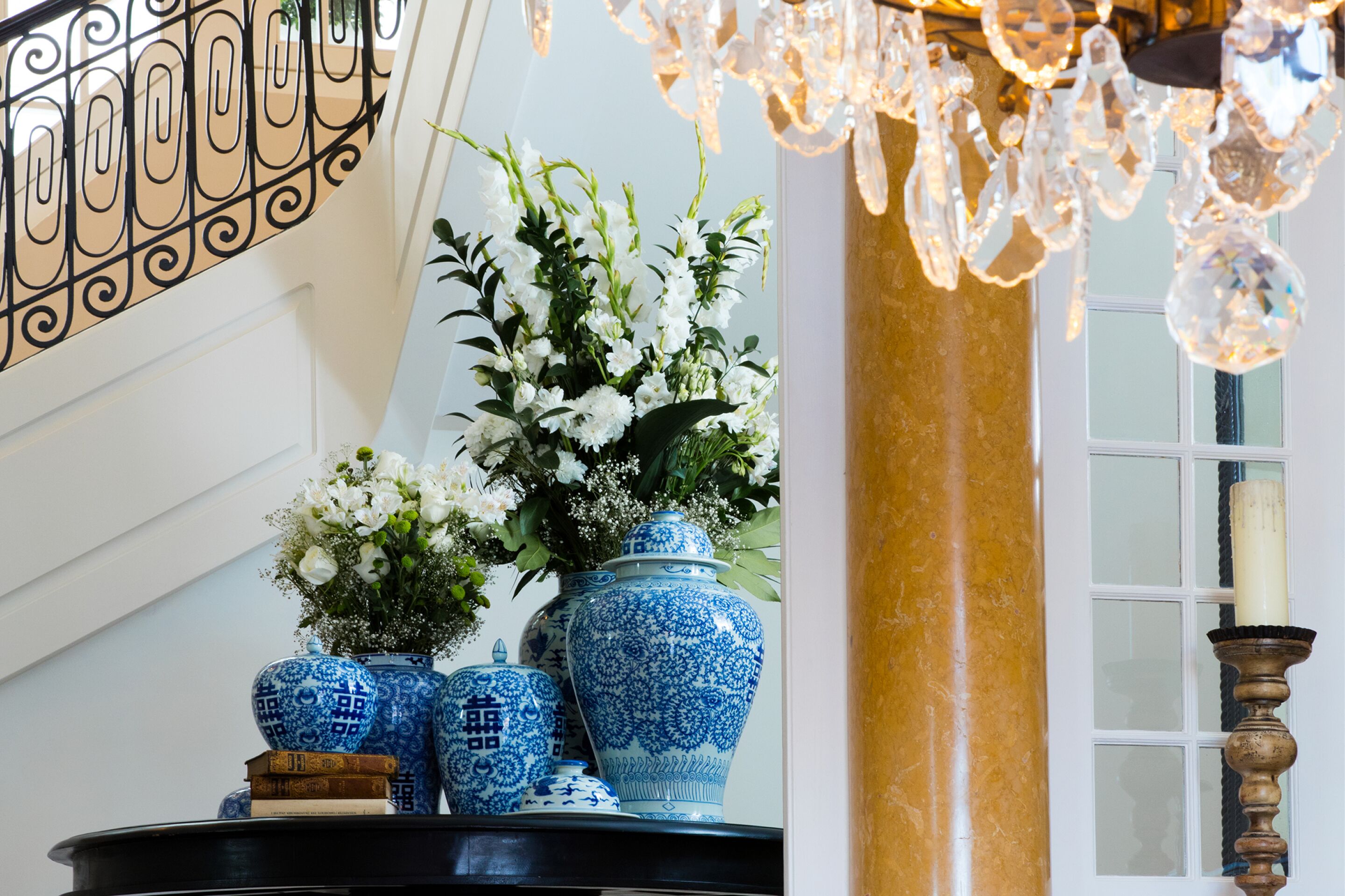 Una escalera con barandilla decorativa, un jarrón con flores blancas y un candelabro.