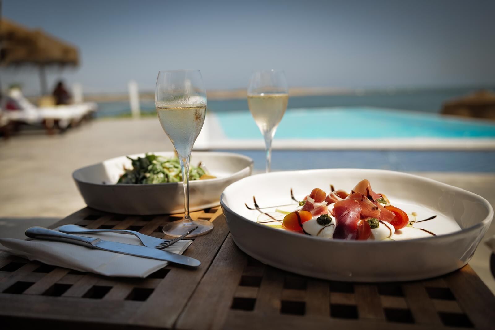 A dining table with a plate of food, two glasses of white wine, and a bowl of salad.