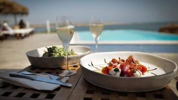 A dining table with a plate of food, two glasses of white wine, and a bowl of salad.
