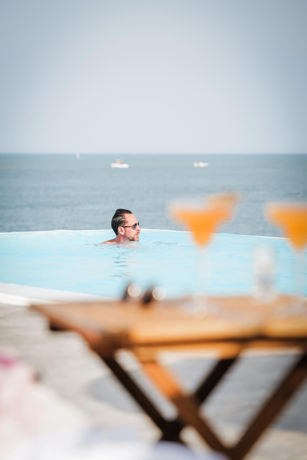 A person in a swimming pool with a view of the ocean and a bar area with two martini glasses.