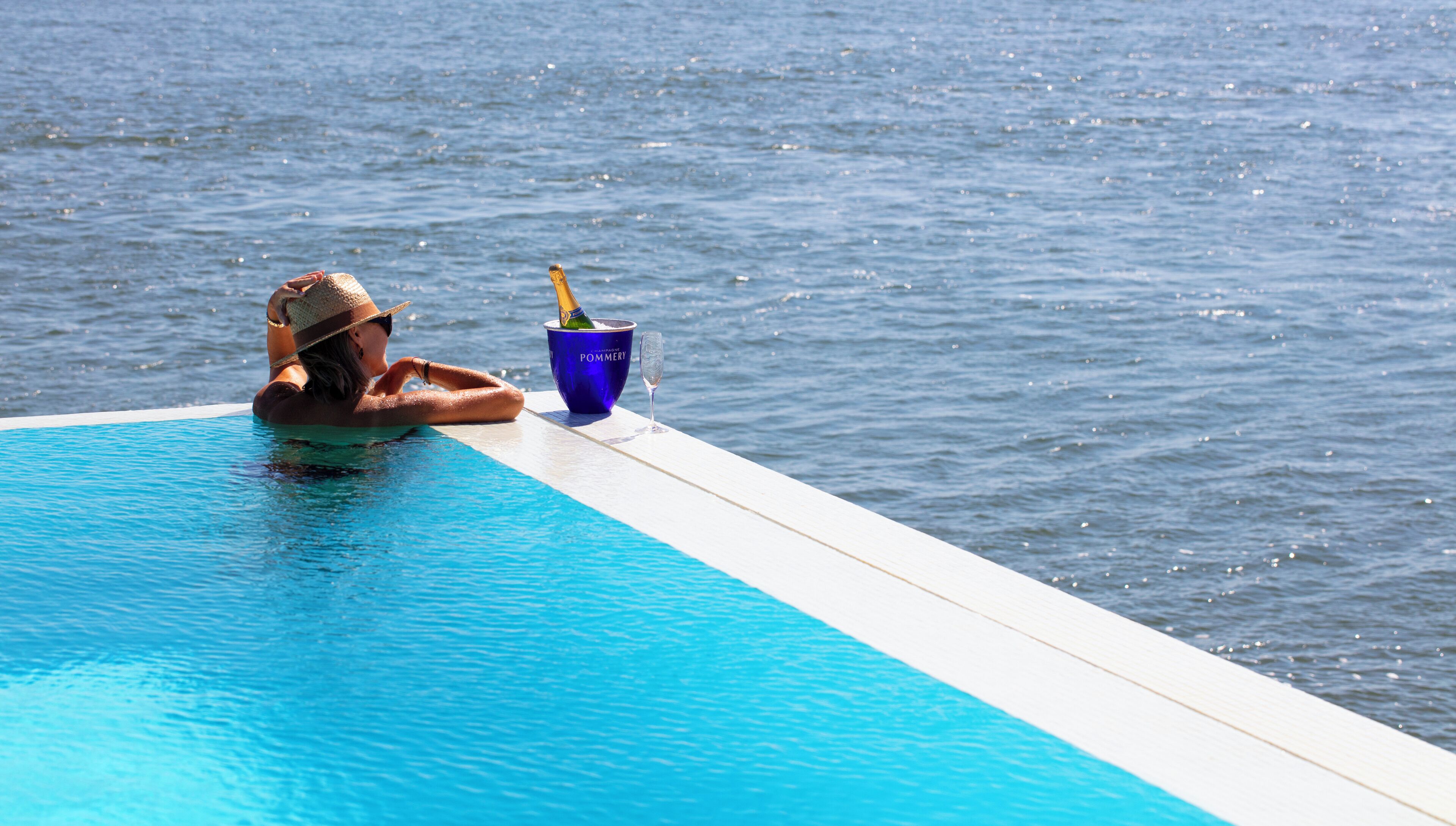 Una persona si rilassa a bordo piscina con un drink e un bicchiere.