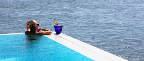 A person relaxing by a pool with a drink and a glass.