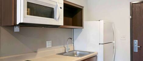 A compact kitchen with a built-in microwave, a stainless steel sink, and a white refrigerator.