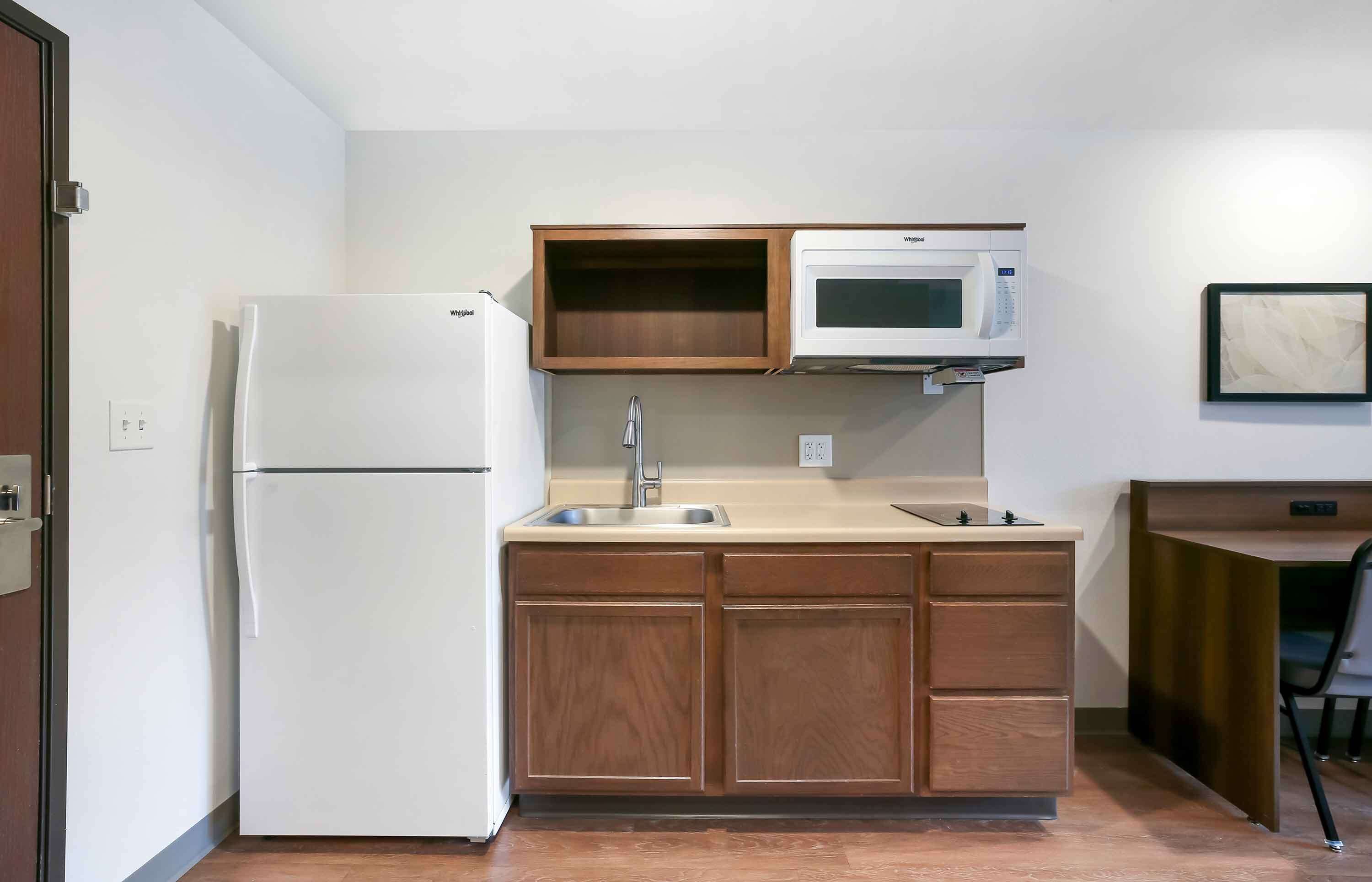Una cocina compacta con refrigerador, microondas, pileta y alacenas de madera.