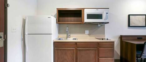 Una cocina compacta con refrigerador, microondas, pileta y alacenas de madera.
