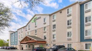 A multi-story hotel with a stone facade, a green logo, and a parking lot with several cars. - Extended Stay America Suites - Providence (Providence)