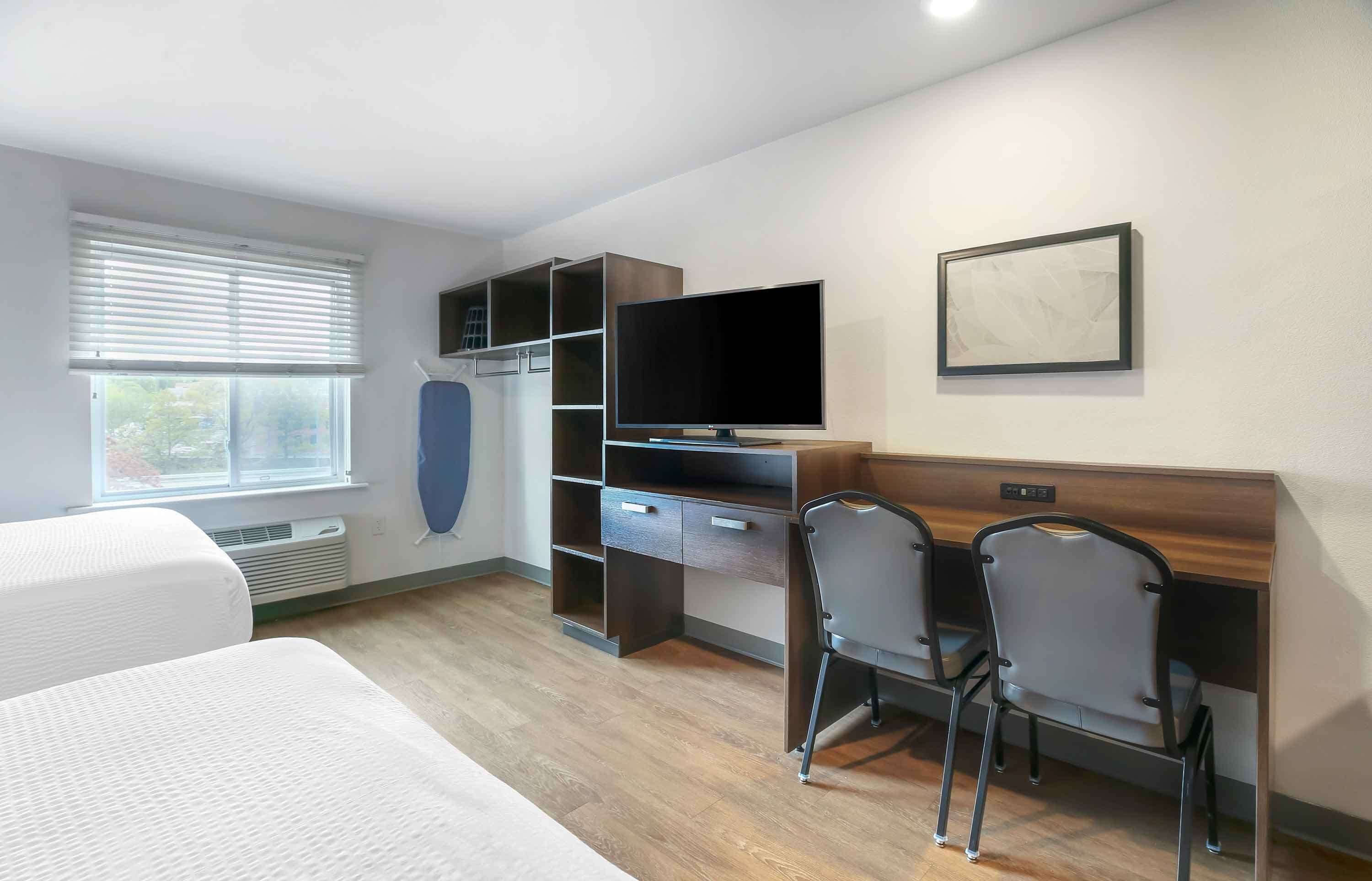 A hotel room with a bed, a desk with a computer, a TV, and a window with blinds.