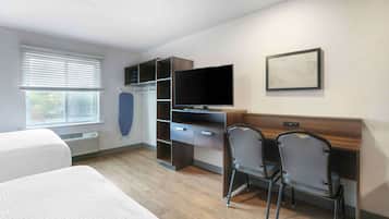 A hotel room with a bed, a desk with a computer, a TV, and a window with blinds.