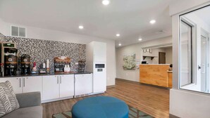 A modern kitchen with white cabinets, a coffee station, and a blue ottoman. - Extended Stay America Suites - Providence (Providence)
