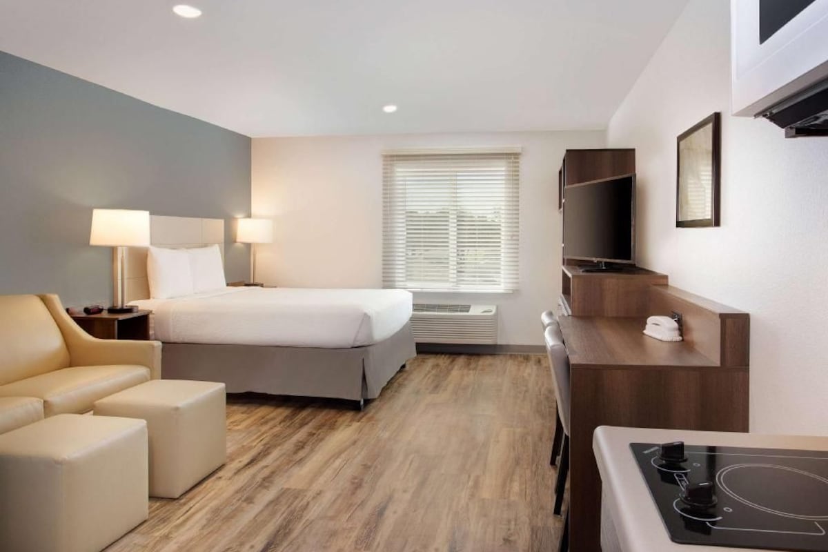 A hotel room with a bed, a desk, a chair, a TV, and a small kitchenette.