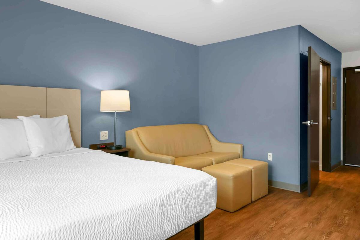 Una habitación de hotel con una cama grande, un sillón color beige y un pequeño reposapiés.