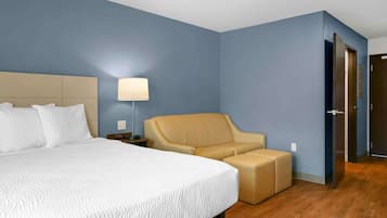 A hotel room with a large bed, a beige armchair, and a small ottoman.