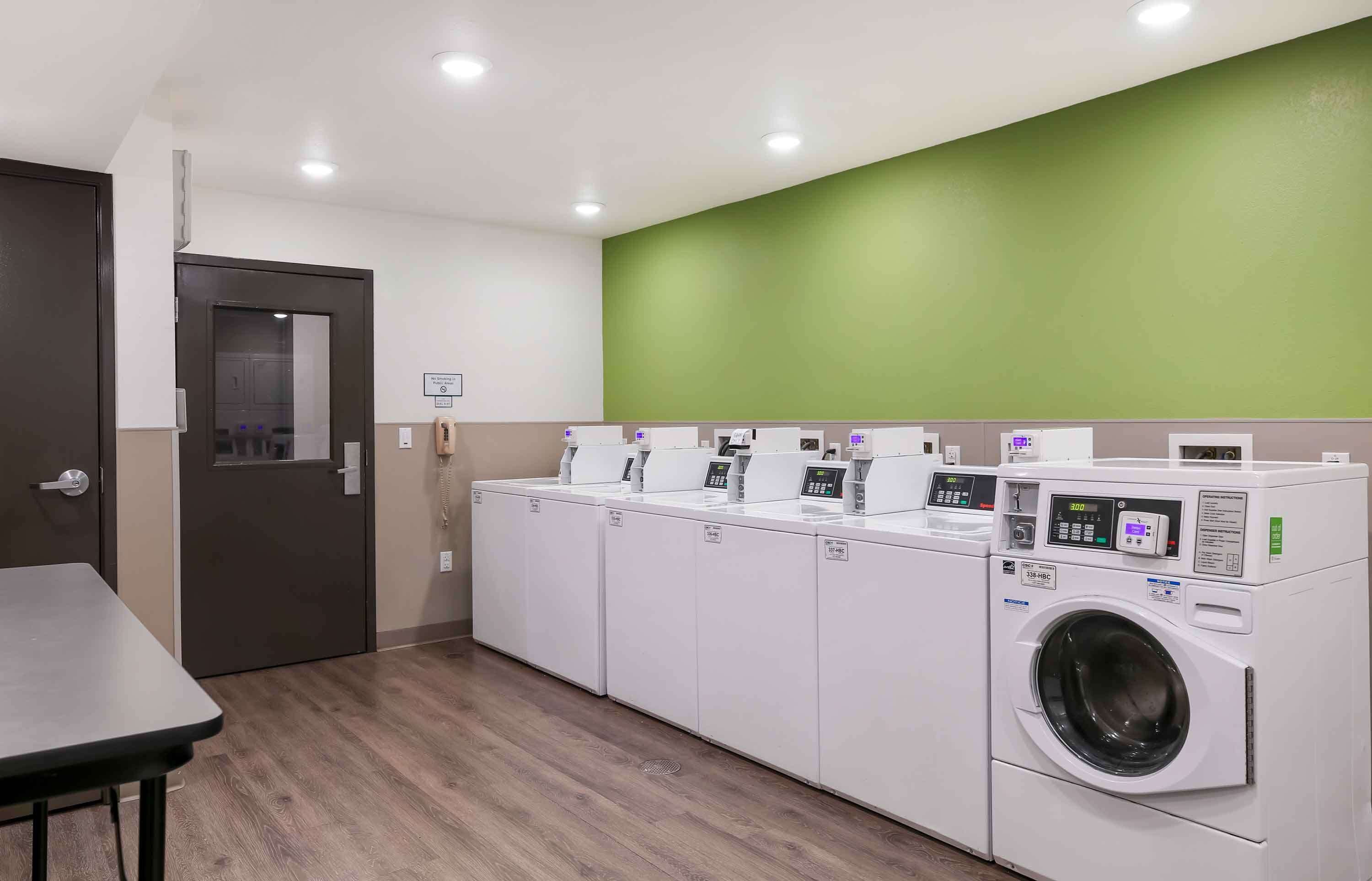 Une buanderie équipée de quatre machines à laver et d’un sèche-linge, ainsi que d’une table et d’une porte.
