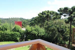 A view from a balcony overlooking a lush green landscape with dense trees and a distant red building.