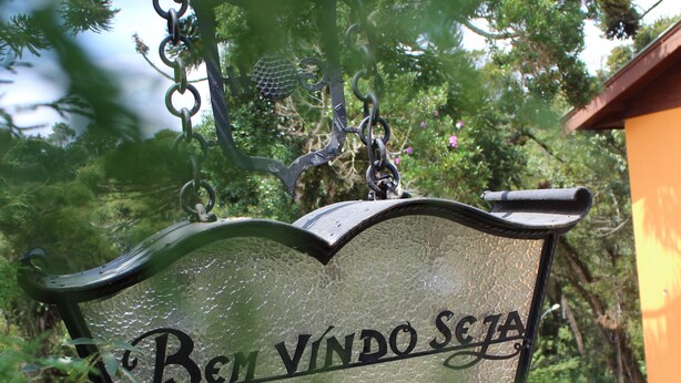 A sign with the text "Bem Vindo Seja" in a garden setting. - Recanto Brumas (Campos do Jordão)