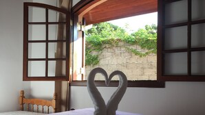 A bed with a heart-shaped towel arrangement, a wooden headboard, and a window with a view of greenery. - Recanto Brumas (Campos do Jordão)