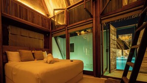 Quarto com uma cama grande, cabeceira de madeira e vista para uma piscina interior através de uma porta de vidro.