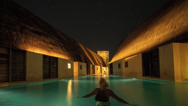 Uma pessoa caminhando em uma área de piscina com céu noturno visível acima.