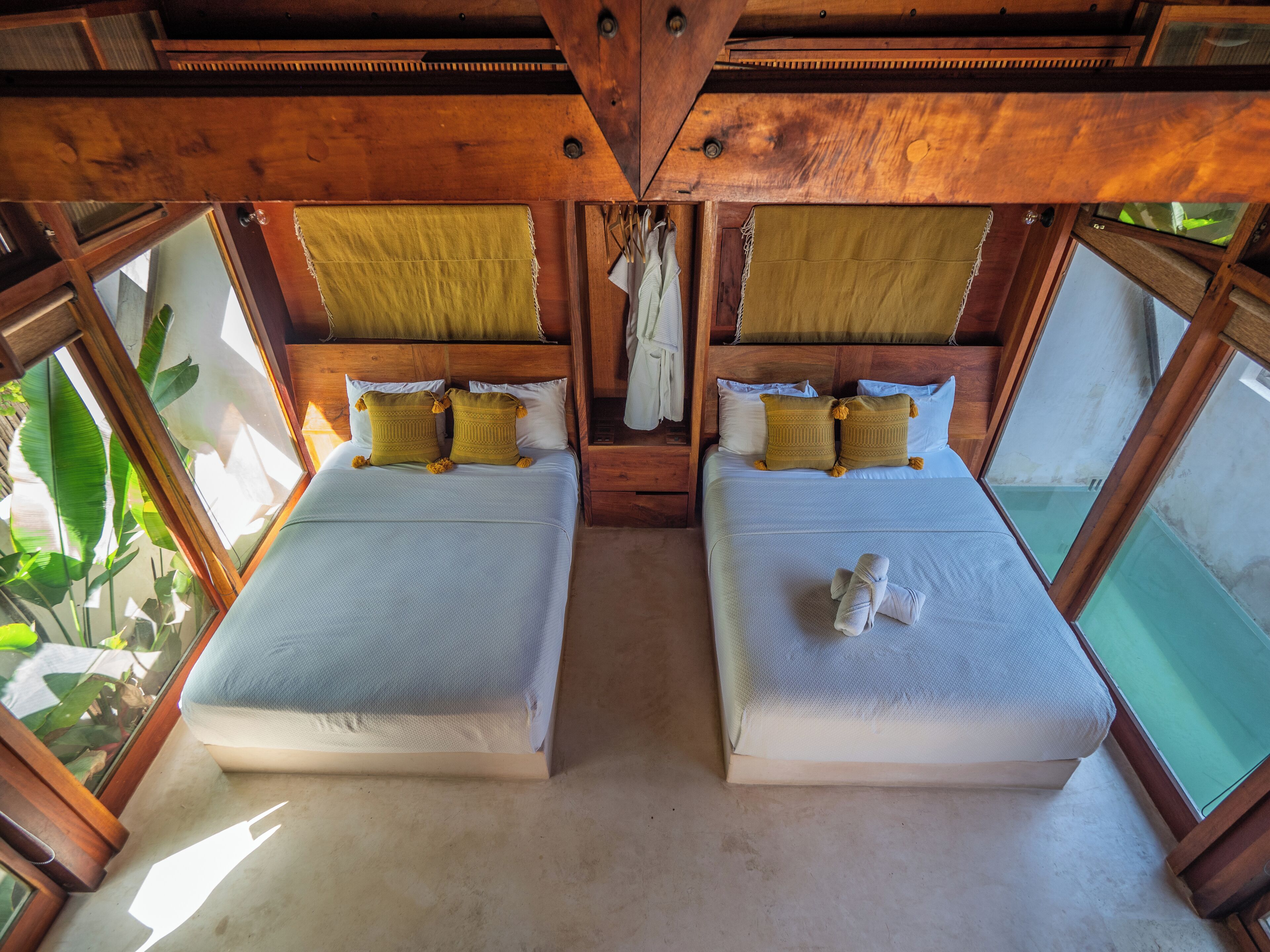 A room with two beds, wooden ceiling beams, and large windows.