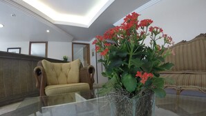 A lobby with a glass-top table, a sofa, and a decorative plant with red flowers. - Residencial Porto Farol (Salvador)