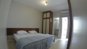 A bedroom with a bed, a bedside table, and a mirror. - Residencial Porto Farol (Salvador)