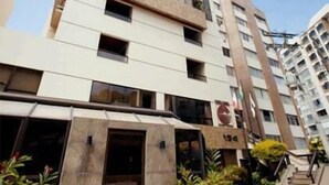 A multi-story building with a modern architectural design, featuring a mix of beige and white exterior walls, large windows, and a visible entrance with a staircase leading to the ground level. - Residencial Porto Farol (Salvador)