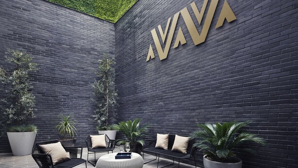 A modern outdoor seating area with black metal chairs and ottomans, surrounded by large potted plants and a dark brick wall with a large gold logo. - Felix Luxury Plus by Viadora (Mexico City)