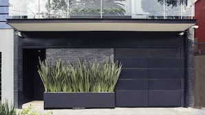 A modern garage with a dark facade, a large planter with tall plants, and a glass balcony above. - Felix Luxury Plus by Viadora (Mexico City)