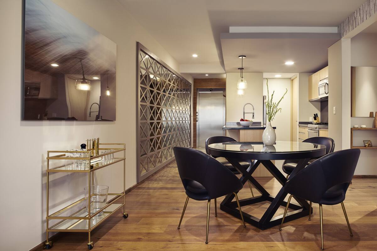 A modern dining area with a round table, dark chairs, and a gold-framed glassware cart.