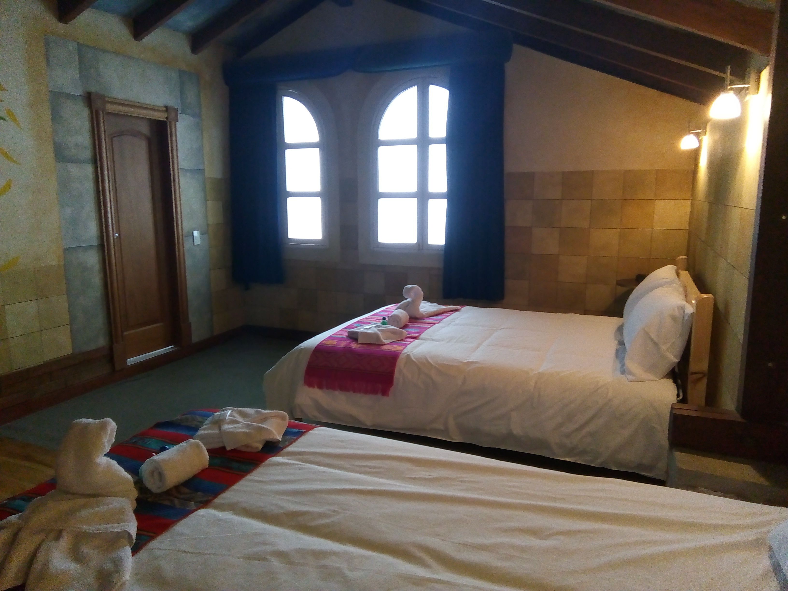 A hotel room with two beds, a wooden door, and two windows with curtains.