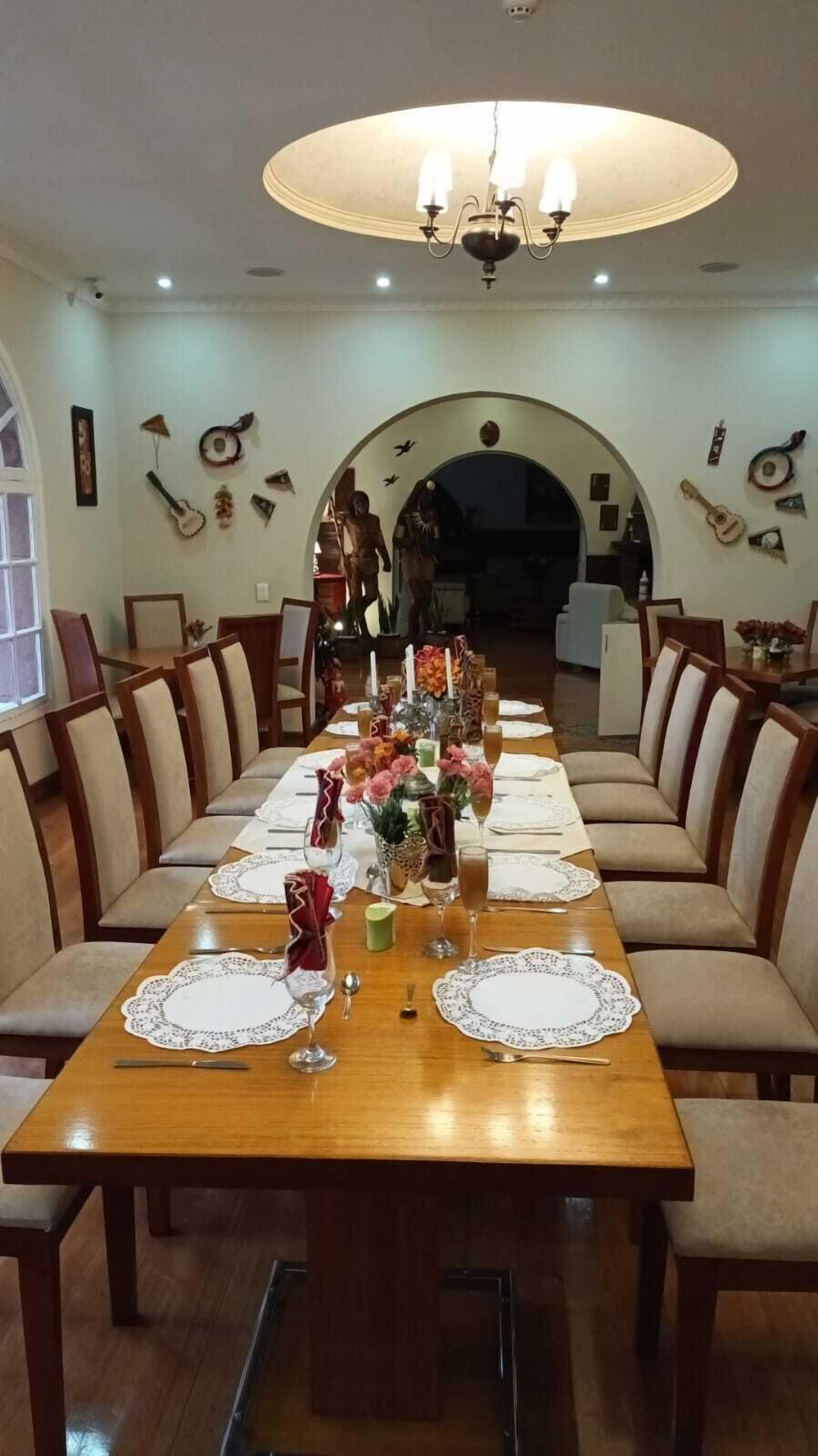 Un comedor con una larga mesa de madera dispuesta para una comida, rodeado de sillas tapizadas.