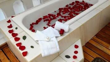 A bathtub filled with rose petals and a white towel.