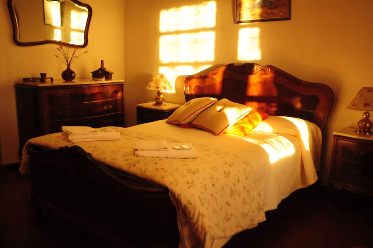 Ein ordentlich bezogenes Bett mit einer floralen Tagesdecke, einer Nachttischlampe und einem Nachttisch mit einer Vase und einer Lampe.