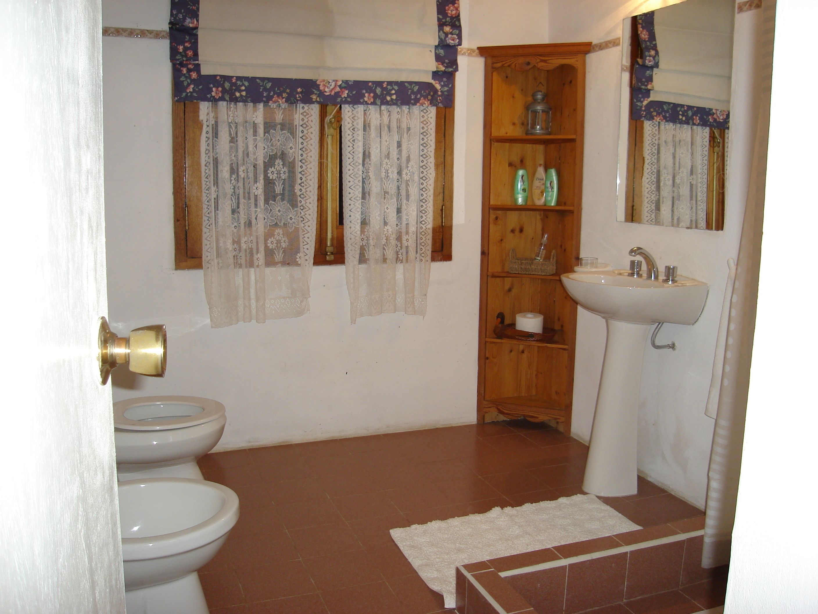 A bathroom with a toilet, sink, and wooden shelf with toiletries.