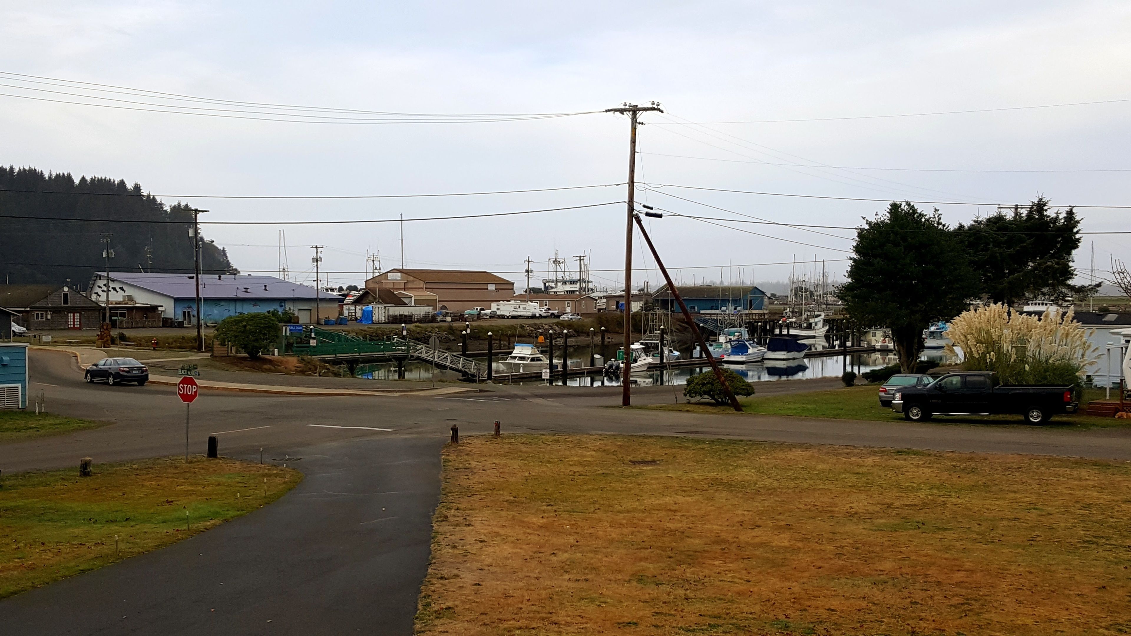 A coastal road with a stop sign, a bridge, and a marina with boats.