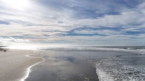 A beach with a wide sandy shore, gentle waves, and a partly cloudy sky. - Winchester Bay Inn (Reedsport)