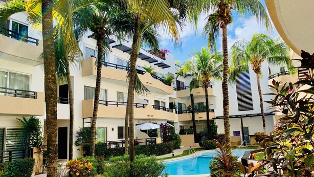 A multi-story hotel with a swimming pool surrounded by palm trees and lush greenery. - Condo Pacifico by Playa Paradise (Playa del Carmen)